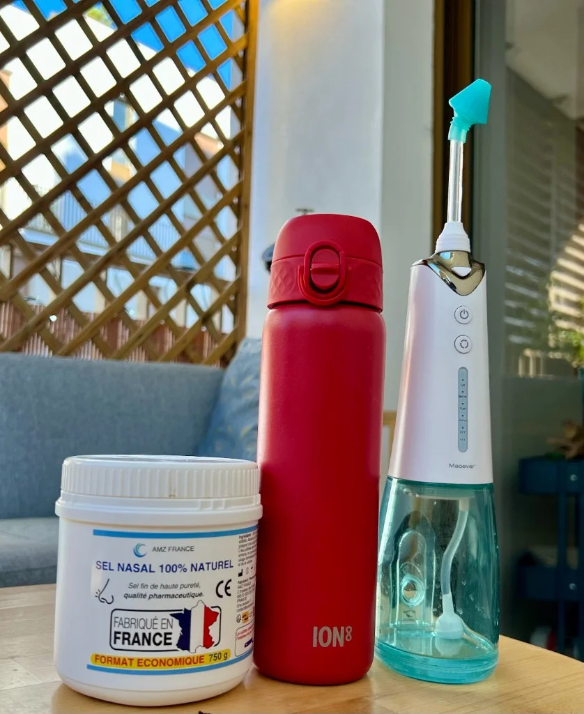 Verre d'eau tiède, pot de sel nasal et machine de lavage nasal sur un comptoir de salle de bain